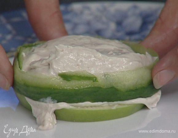 С огурца снять кожицу таким образом, чтобы получилась длинная зеленая ленточка шириной примерно 1 см, и опоясать ею селедочную массу, которая находится между яблоками.