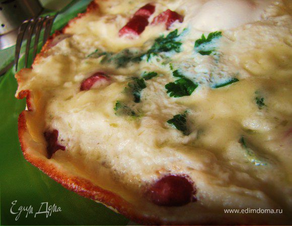 Залить колбаски яйцами, закрыть сковороду крышкой  и жарить омлет до пышности. За пару минут до готовности, когда омлет поднимется, засыпать его тертым сыром.