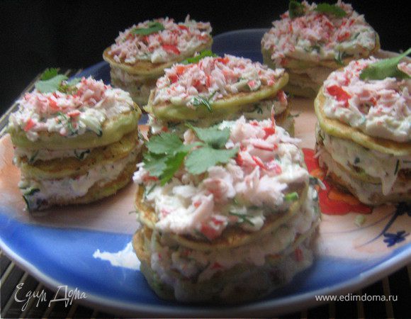 Кабачки вымыть,отрезать кончики,не чистить,натереть на крупной тёрке,добавить яйца,молоко,соль,сахар,перец,хорошо размешать,всыпать муку,мешать,добавляя муку, что бы тесто было как густая сметана,добавить раст,масло.На хорошо разогретую сковородку ложкой выкладывать оладьи и жарить с двух сторон до готовности.Готовые оладьи охладить.Сделать начинку:натереть на тёрке крабовые палочки(отложить не много крабовой "стружки" для украшения)добавить тёртый огурец,измельчённый чеснок,плавленный сыр,нарубленный укроп,всё хорошо размешать,посолить,поперчить по вкусу.Оладьи намазать крабовой начинкой,сложить друг на друга "башенкой",верх тоже намазать начинкой и посыпать крабовой "стружкой",украсить зеленью,поставить на часок-другой в холодильник.