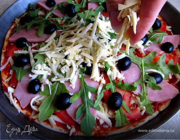 На слой сыра выкладываем тонко порезанные томаты, ветчину, украшаем рукколой и оливочками. Сверху посыпаем еще раз сыром, но не много.
