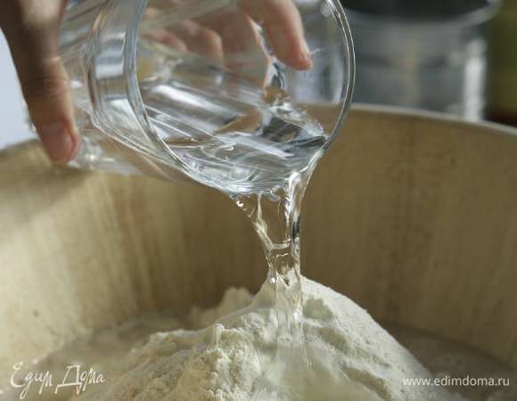 Влить 700 мл теплой воды (20°С) и вымешивать большой деревянной ложкой. Если тесто получается слишком крутым, добавить еще немного воды.