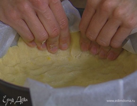 Разъемную форму для выпечки (20 см) выстелить пекарской бумагой, выложить 2/3 теста и равномерно его распределить, чтобы получились бортики до середины формы.