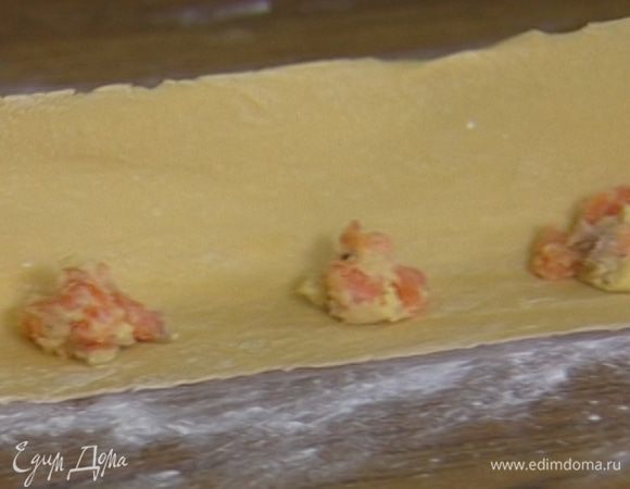 Отдохнувшее тесто выложить на рабочую поверхность, присыпанную мукой, раскатать его скалкой в тонкий пласт (можно использовать специальную машинку для пасты). На одну половину теста на некотором расстоянии друг от друга выложить по пол чайной ложки рыбной начинки.