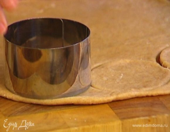 Вырезать формочкой или стаканом из теста кружки, а затем сделать в них выемки посередине с помощью формочки меньшего диаметра.
