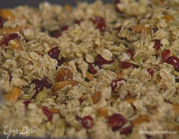 Глубокий противень смазать маслом и выложить на него овсяные хлопья с семечками и клюквой. Равномерно распределить ложкой.  