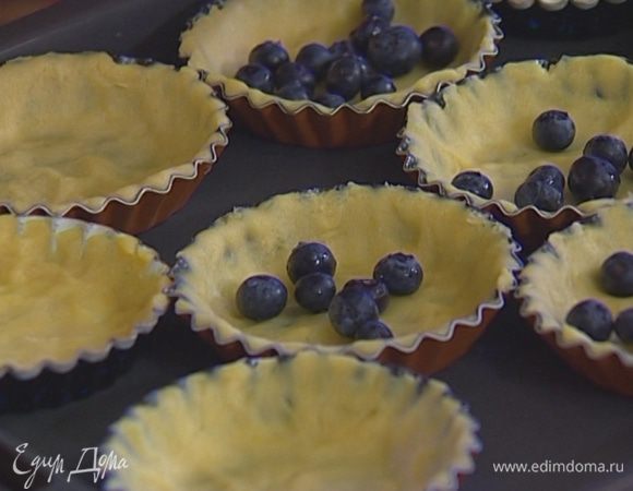 Поместить тарталетки с тестом на противень. На дно каждой тарталетки выложить немного ягод. 