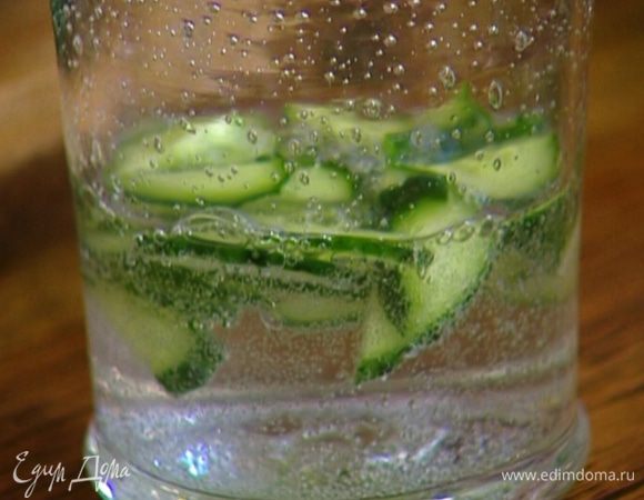 Половинку огурца нарезать небольшими кусочками, выложить в прозрачный стакан и залить минеральной водой.