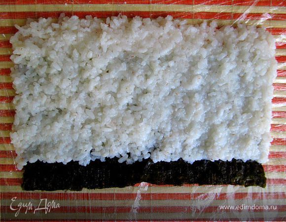 Рис выкладывается сверху за пределы листа нори, снизу оставляем 2см без риса. (Если потребуется, мойте руки в миске с водой и лимоном, чтобы взять новую порцию риса)