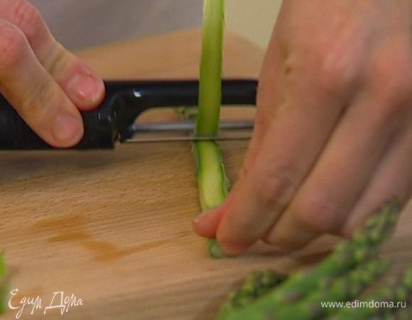 У трех стеблей спаржи отломить грубые верхние части, а саму спаржу порезать картофелечисткой на длинные тонкие ленточки.