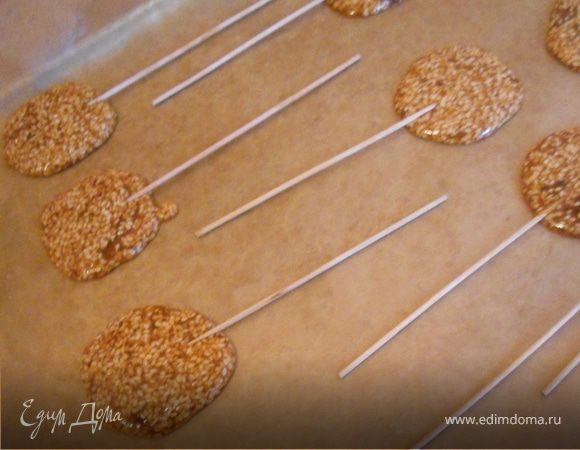 Подготовить бумагу для выпечки. Чайной ложкой выложить небольшое количество массы, разровнять и придать необходимую форму. Вставить палочку и поверх нее - еще несколько капель карамели, для надежности. Карамель достаточно быстро твердеет, ее можно быстро прогреть и продолжить создание леденцов. Оставить до полного застывания при комнатной температуре. П.С. Интересно так, несмотря на форму, это не только детское развлечение:) Почти кунжутные козинаки. П.П.С. Опасался, что с одной стороны конфеты будут декорированы аппликацией, поэтому часть бумаги смазал маслом. Совершенно не нужный пункт, т.к. отходят совершенно прелестно:))