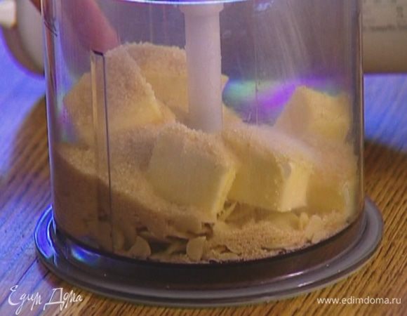 Оставшееся масло порезать кубиками, выложить в блендер, добавить часть миндальных хлопьев, оставшийся сахар и все взбить. 