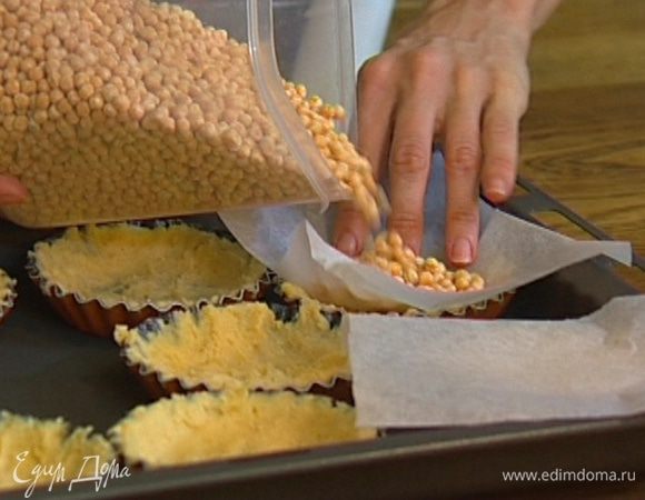 Из бумаги для выпечки вырезать квадраты по количеству и размеру тарталеток, выложить бумагу на тесто и насыпать сверху горох. 