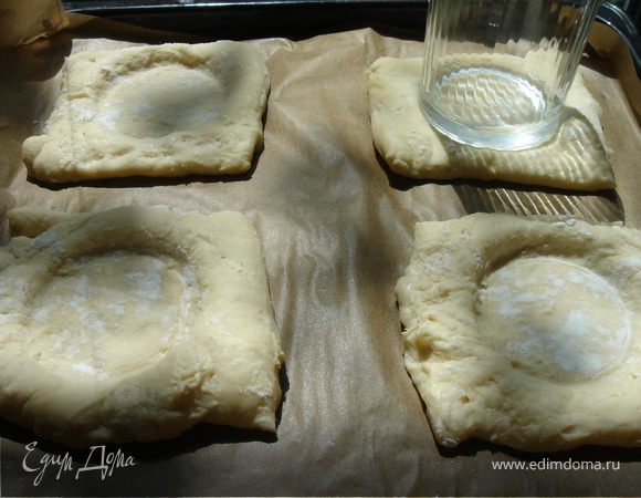 Тесто немного разморозить и разрезать каждый пласт на 4 квадрата.Противень застелить бумагой для выпечки.Выложить квадраты на противень,прикрыть полотенцем и ставить на расстойку.Когда тесто достаточно поднимется,придавите середину смазанным растительным маслом дном стакана.