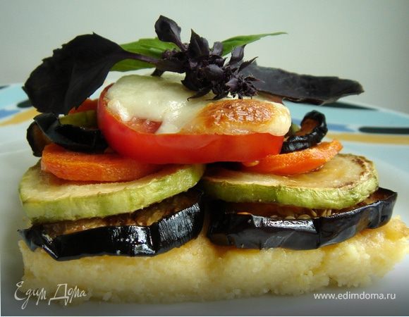 Жаропрочную форму застелить бумагой для выпечки,выложить в неё кукурузную кашу и разровнять.Овощи,кроме помидор, порезать произвольно и обжарить раздельно на растительном масле.Выложить овощи на кукурузную кашу,немного посолить,поверх овощей разложить кружки помидор.Засыпать тёртым сыром.Выпекать около 10-20 минут до готовности сыра.Ломтики бекона обжарить на сухой сковороде на сильном огне.Готовую поленту разрезать на порции.Подавать с хрустящим беконом и любимой зеленью.Приятного аппетита!