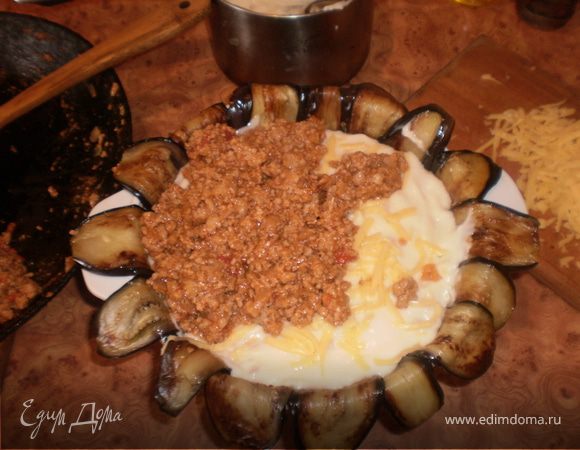 Огнеупорную форму выкладываем баклажанами (дно и стенки, полоски со стенки должны оставаться свободными, ими накроем мусакас сверху). Поочередно выкладываем слои мясного фарша и соуса (слой соуса делайте толстым, чтобы его было хорошо видно в разрезе, что у меня получилось не везде). Посыпаем натертым сыром и накрываем баклажанами.