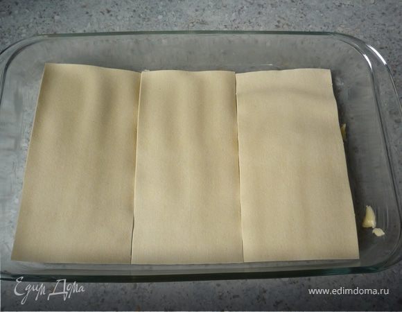 Разогореть духовку до 200°C. Форму для запекания смазать маслом. Выложить 3 листа лазаньи, сверху распределить 1/3 начинки.