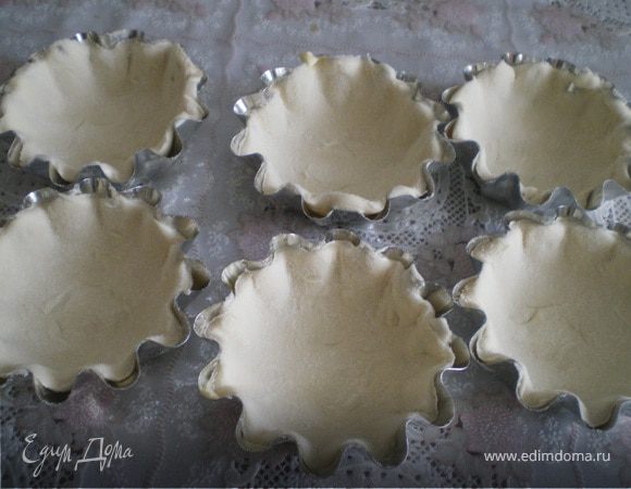 Формочки для тарталеток смазать маслом. Тесто раскатать в пласт, вырезать из него кружки, выложить в формочки и сделать вилкой частые проколы на поверхности. Лишнее тесто срезать.