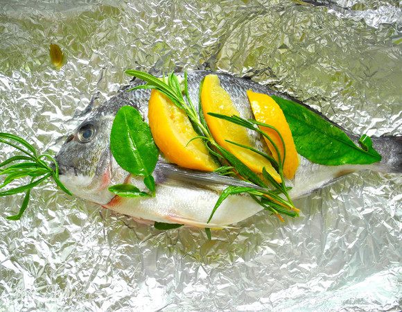 Четвертинку лимона и часть трав положить в пузико. Сверху рыбку надрезать поперек туловища, и положить в разрезики дольки соленого лимона. Сверху украсить травами и листьями лимона. Сбрызнуть оливковым маслом. 