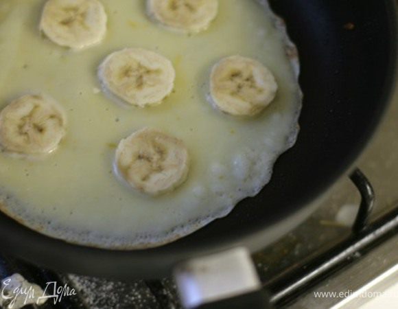 На сковородку наливайте тесто и сразу кладите кусочки бананов, пока блин не схватился. Если сковорода не тефлоновая, в тесто заранее добавьте ложку растительного масла.