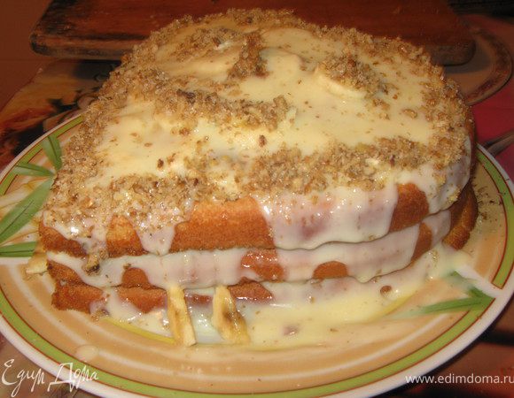 Готовые коржи смазать кремом и между каждым выложить нарезание бананы. Сверху залить оставшимся кремом и украсить орехами.