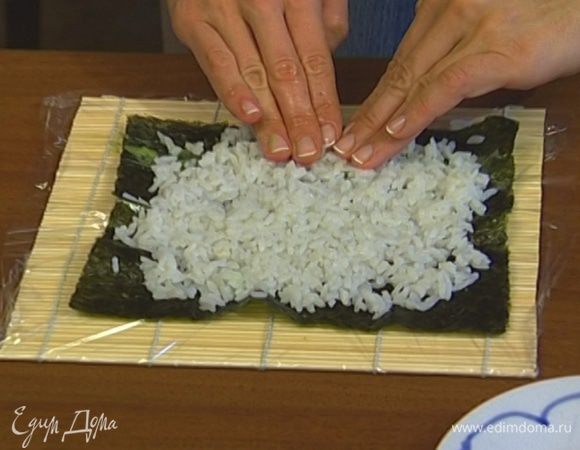 Застелить коврик для суши пищевой пленкой, сверху положить лист нори, один длинный край бумаги намазать васаби, выложить на бумагу рис и утрамбовать его (чтобы рис не прилипал к пальцам, можно смочить руки в воде с уксусом или лимоном). 