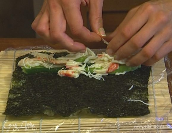 Перевернуть лист с рисом таким образом, чтобы рис оказался на покрытом пленкой коврике. Выложить сверху огурец, авокадо и крабовое мясо. 