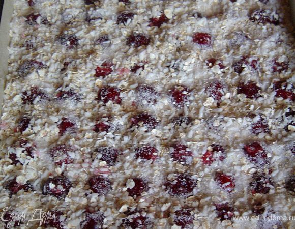 Тесто выкладываем на противень, застеленный пекарской бумагой. Сверху кладем вишню, слегка вдавливая в тесто. Немного кокосовой стружки, сахара и овсяных хлопьев перемешиваем. Равномерно посыпаем сухой смесью вишню. Затем отправляем все в разогретую до 190°C духовку и выпекаем пирог 35–40 минут. 