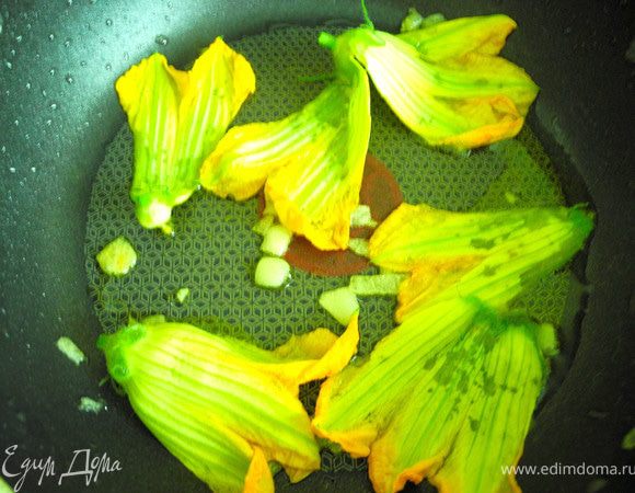 Нарезать чеснок, добавить его в нагретую сковороду с маслом, обжарить в течение нескольких секунд, выложить цветки тыквы (цуккини) на сковороду.