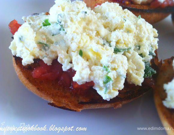 Тосты полить соусом из томатов, выложить кусочки томатов. На каждую булочку выложить по одной столовой ложке творога. Размазать аккуратно ножом. 