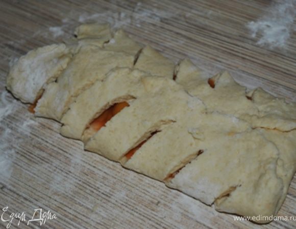 В центр пласта положите абрикосы, оставив свободными края шириной 5 см с каждой стороны. Заверните узкие края с обеих сторон, частично прикрыв начинку.
Заверните эти полосы, накрыв начинку так, чтобы края сошлись в серединке.