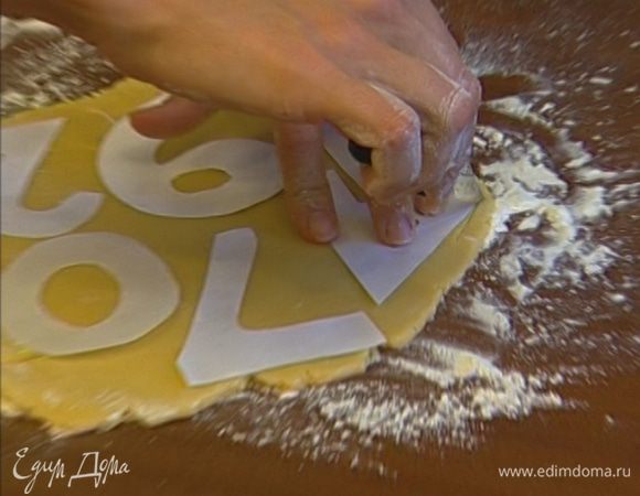 Раскатать тесто в пласт толщиной примерно 5 мм и вырезать из него печенье с помощью рюмки или специальных формочек (интересный вариант — сделать из бумаги цифры и, положив их на тесто, вырезать ножом печенье в форме цифр).