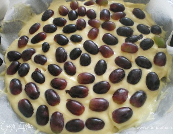 Форму для выпечки смазать сливочным маслом. На дно формы налить половину теста, сверху выложить дольки яблок. Залить оставшимся тестом. Верх украсить виноградом, разрезанным пополам.