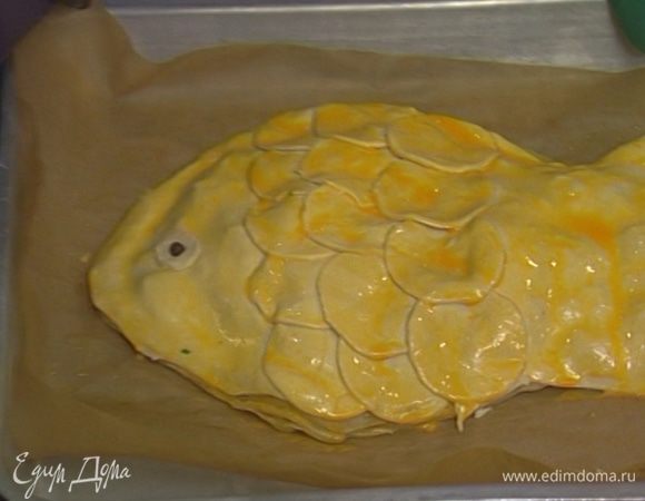 Выложить начинку на пропеченное тесто и равномерно распределить. Сверху положить вырезанные из теста нос и хвост рыбы, все туловище выложить кружками, укладывая их друг на друга так, чтобы получилась «чешуя». Смазать всю поверхность желтком. 