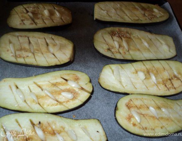 Чеснок очистить, порезать тонкими пластинками. Мелко порезать зелень, помидоры порезать пластинками 5мм, сыр натереть. Баклажаны помыть, очистить от хвостиков, разрезать вдоль пополам. Натереть разрез солью, сделать ножом косые надреза не доходя до шкурки. В разрезы вставить пластинки чеснока, Выложить половинки баклажан на противень.