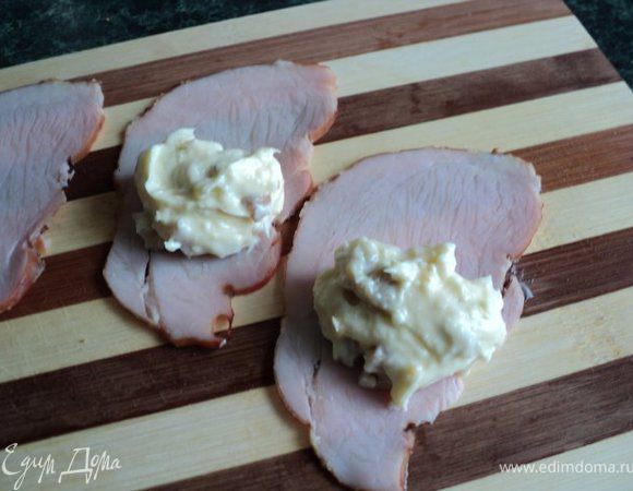 На ломтик ветчины выложить ложку начинки, свернуть рулетиком. Готовые рулетики выложить на блюдо, сверху выдавить кондитерским шприцом сливочный крем, украсить мелкими шампиньонами и зеленью.