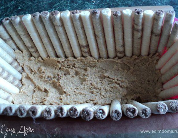 Прямоугольную форму размером 10х20см выстелить бумагой для запекания, чтобы края бумаги свешивались через бортики на 2см ( для облегчения вынимания торта из формы).
На дно выложить смесь печения с маслом, бока торта выложить вафельными трубочками, прижимая их основой торта. Поставить в морозилку на несколько минут для застывания основы.
