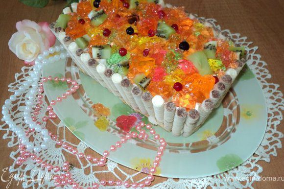 Торт вынуть из формы, освободить от бумаги. Сверху выложить кубики желе, фруктов, ягоды.