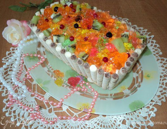 Торт вынуть из формы, освободить от бумаги. Сверху выложить кубики желе, фруктов, ягоды.