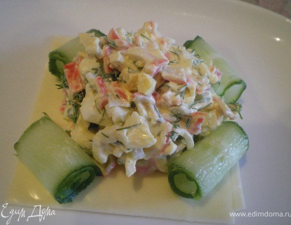 На ломтик сыра выложить салат. Украсить рулетиками из огурца. 