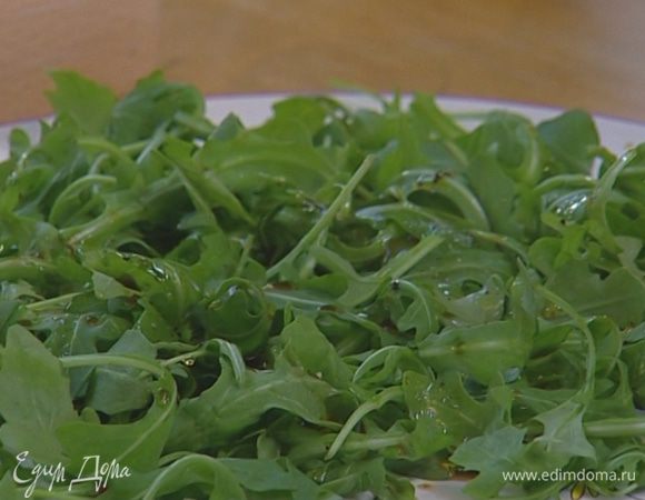 Руколу выложить на большое блюдо и полить небольшим количеством заправки. 