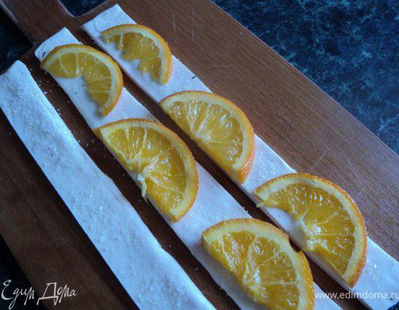Лист готового слоеного теста, развернуть, присыпать немного сахаром, разрезать на полоски шириной 1.5-2см. На каждую полоску положить половинки долек лимона или апельсина, завернуть рулетиком, хорошо прищепнуть край, чтобы при выпечке не развернулся.  