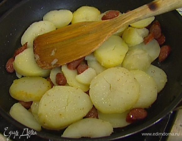 Разогреть в сковороде, которую можно ставить в духовку, растительное масло, обжарить картофель и колбаски до золотистого цвета, затем снять с огня.