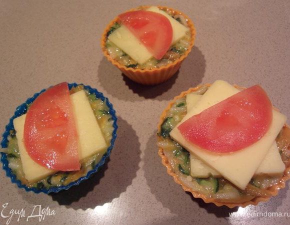 Добавить к массе из риса яйца и сыр (пармезан). Наполнить подготовленные (выложенные пекарской бумагой) формы для маффинов, немного утрамбовать массу. Сверху на каждый маффин положить квадратик сыра и сверху половинку помидорки чери (у меня не было, использовала колечки простого помидорчика, разрезанный на дольки).