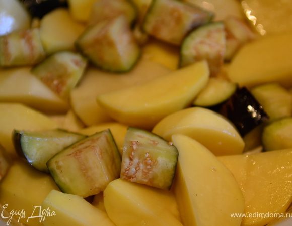 Включить духовку на 230 градусов. Картофель порезать на половинки, а крупные на четвертинки. Баклажаны порезать крупными кусочками. Выложить в форму для запекания.