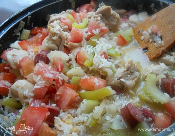 Вернуть к луку, перцу и сельдерею курицу и колбаски, засыпать рис, добавить измельченные томаты. Налить 300-400 мл. воды (можно заменить бульоном), довести до кипения, огонь убавить и далее готовить, регулярно помешивая и добавляя понемногу воды, практически до готовности риса ***лично я предпочитаю состояние аль-денте***. 