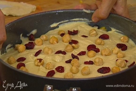 Выложить на фрукты с орехами тесто, присыпать оставшимися дроблеными и целыми орехами и клюквой.