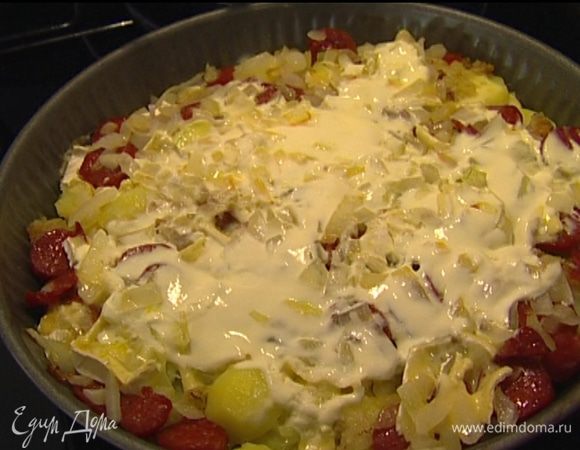 Колбаски, нарезанный кусочками сыр, обжаренные лук и чеснок выложить на картофель с салом, сверху смазать сметаной и отправить на 20 минут в разогретую духовку.