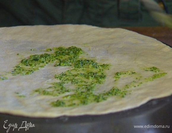 Тесто разделить на две части. Одну часть заморозить, другую раскатать в тонкий пласт, уложить его на перевернутый противень и смазать соусом песто.