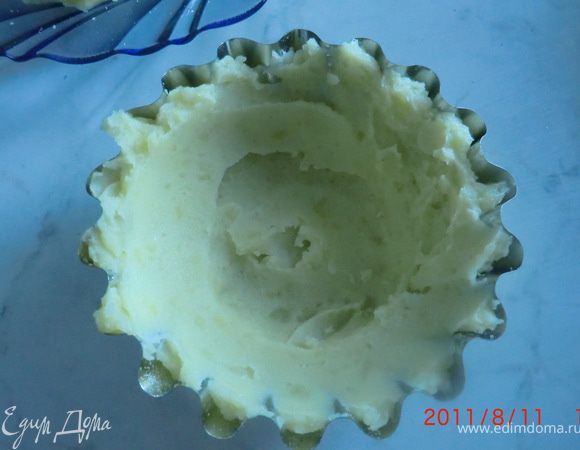 Формочки смазываем маслом и посыпаем панировочными сухарями (можно обойтись без сухарей).Выкладываем картофельное пюре, распределяем его по дну и стенкам формочек.