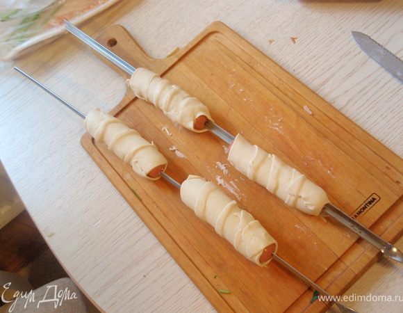 Полосками теста обмотать сосиски обязательно с захлестом. Сосиска увеличивается и немного растягивает тесто.